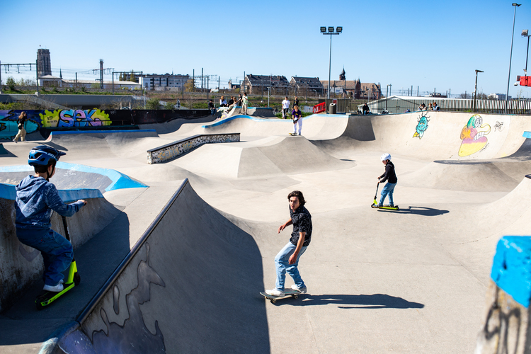 Skatepark met kinderen en tieners die trucjes oefenen op hun skateboard of step.